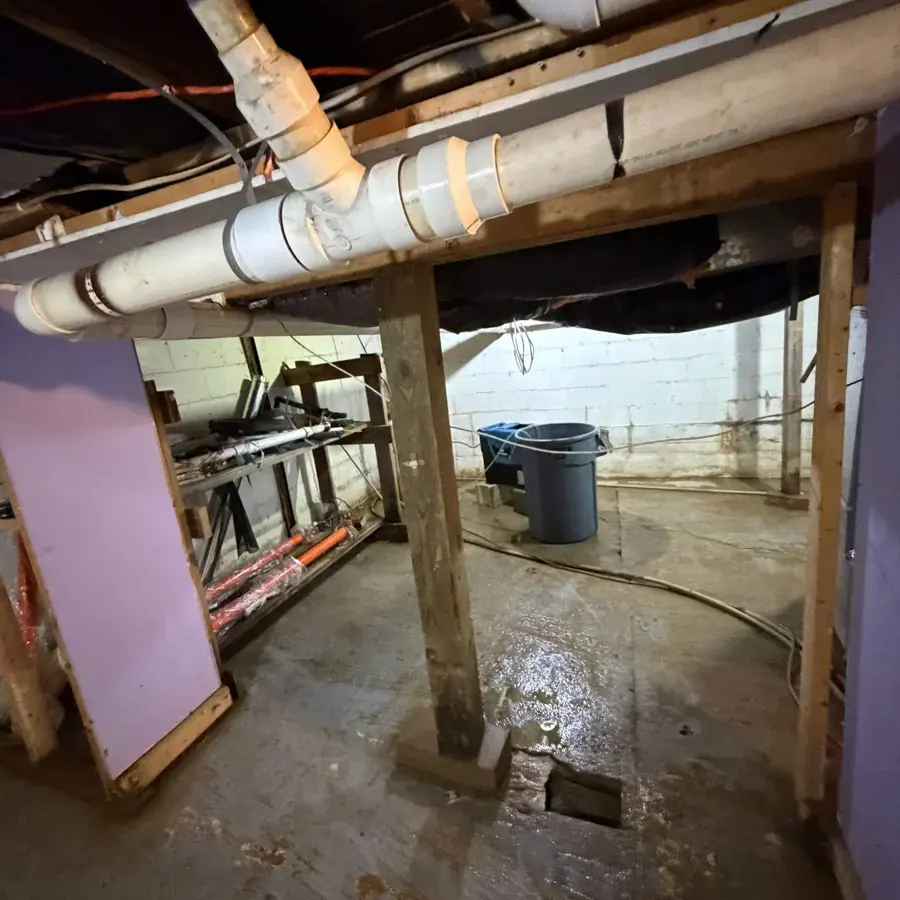 Older basement with exposed joists and pipes over a wet concrete floor