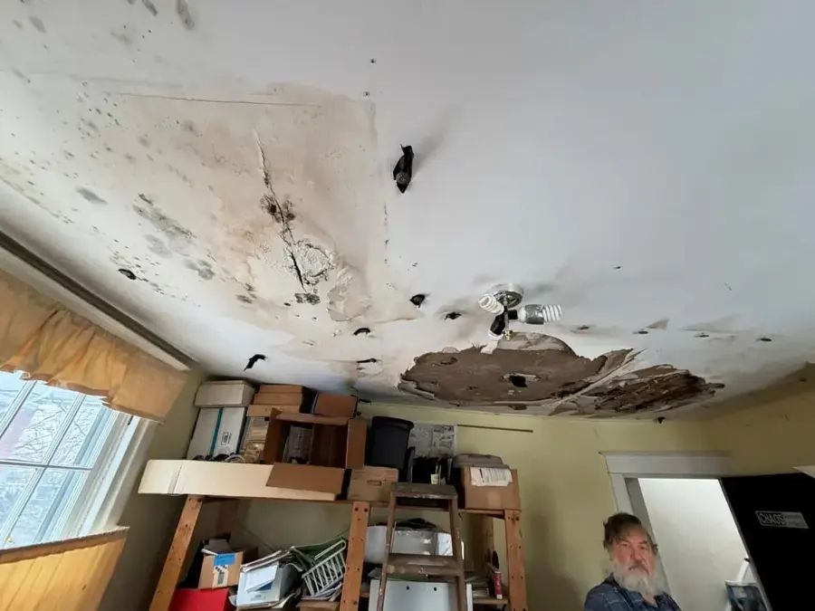 Bedroom ceiling broken open by a roof leak with wet insulation showing